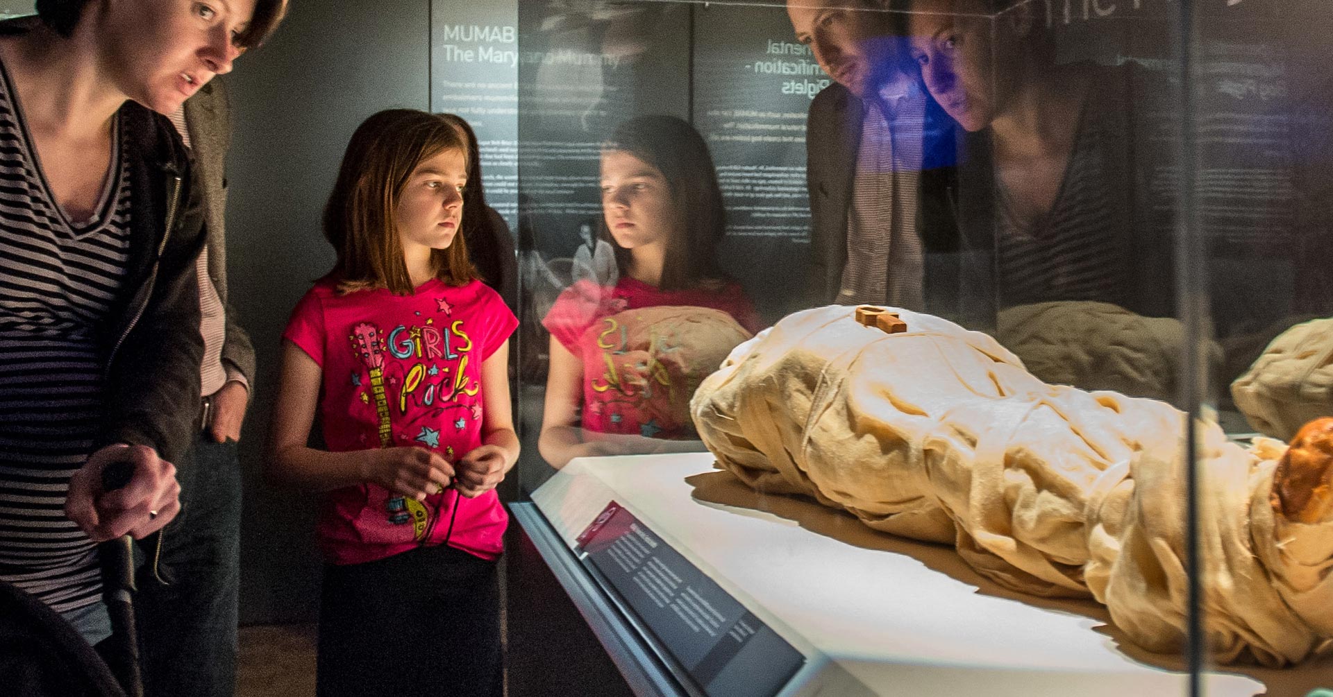 family looks at a mummy on display behind glass